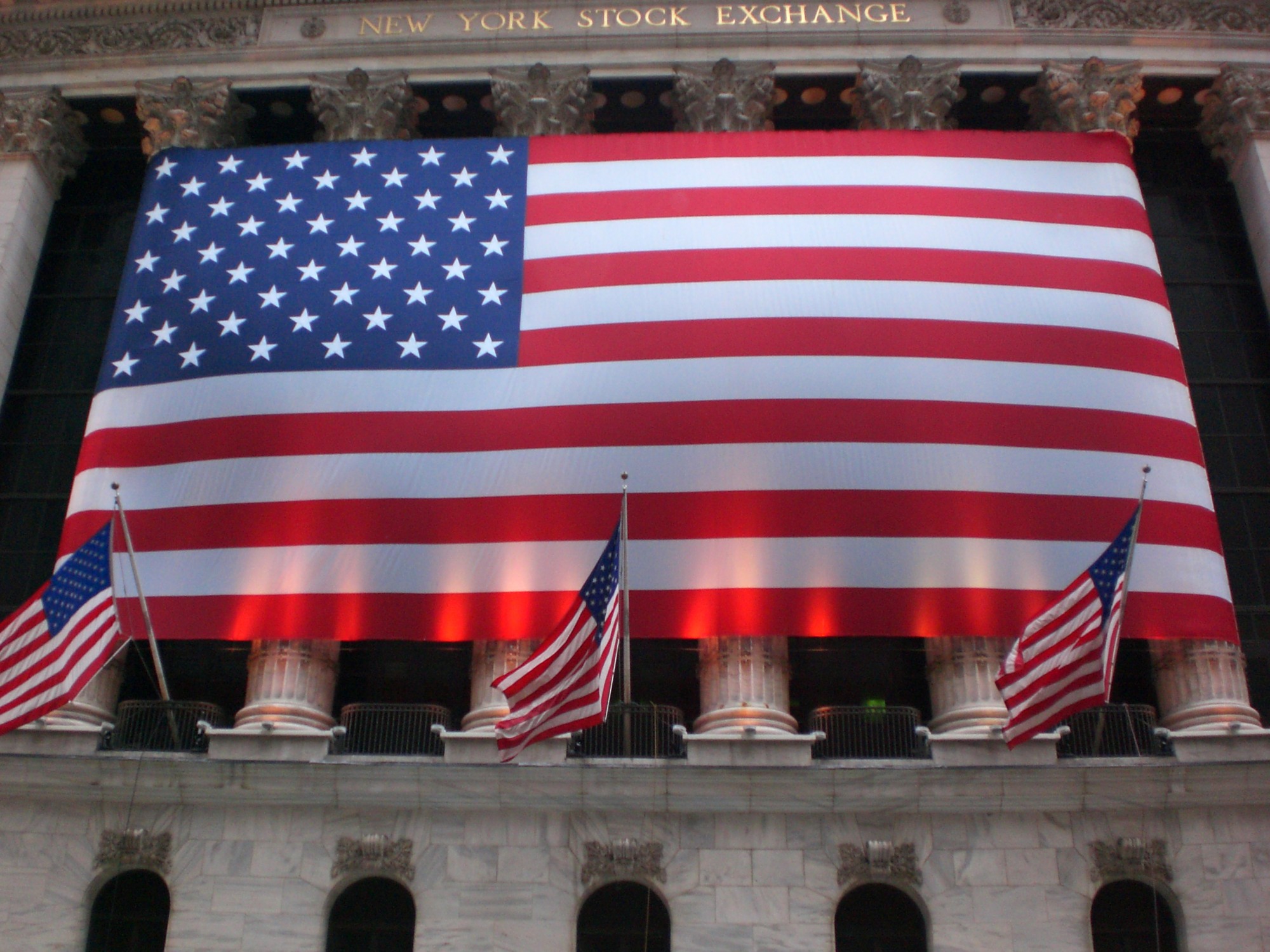 ด้านหน้าอาคาร New York Stock Exchange พร้อมธงสหรัฐฯ เป็นภาพประกอบบริบทตลาดหุ้น